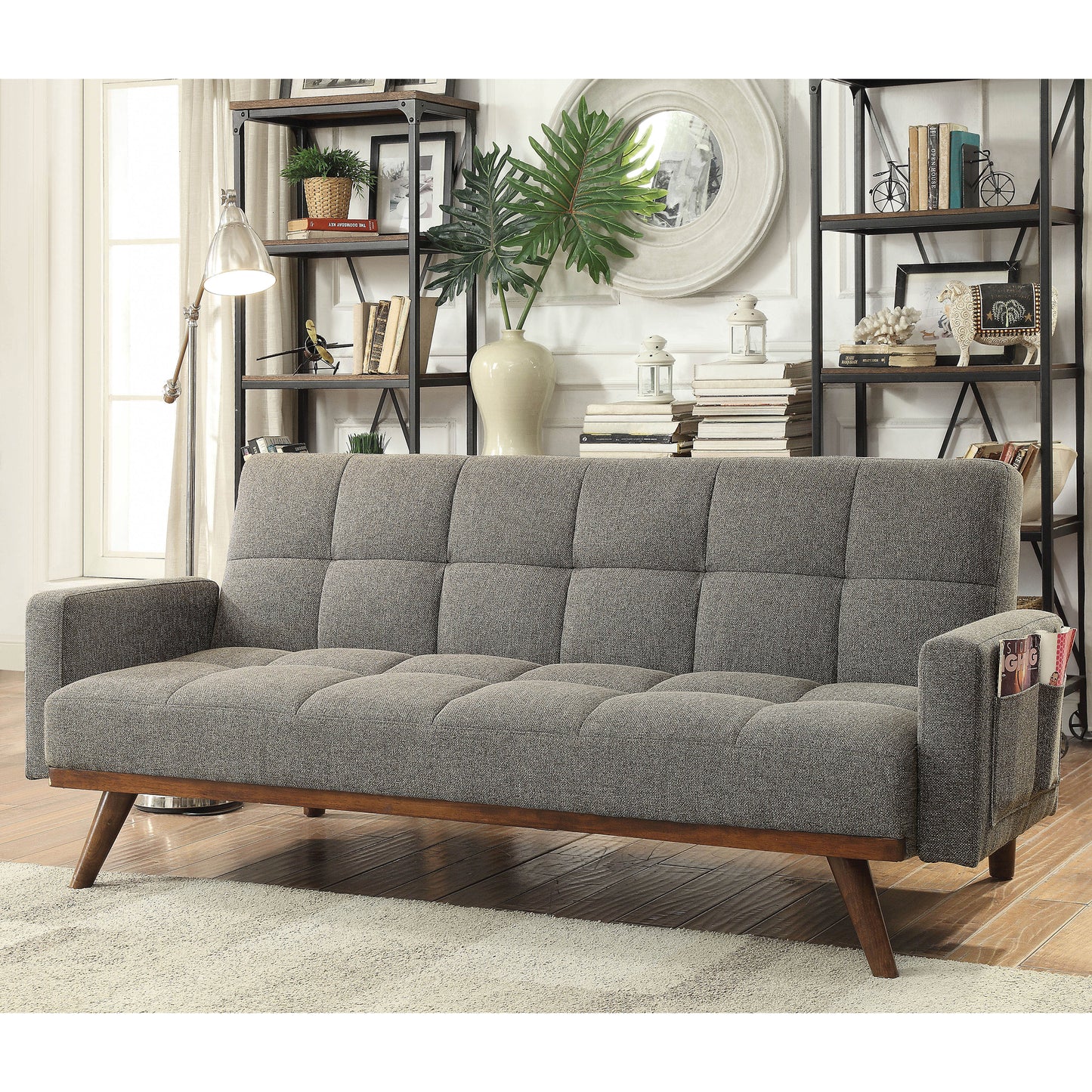Left angled mid-century modern gray tufted futon with a wood base in a living area with accessories