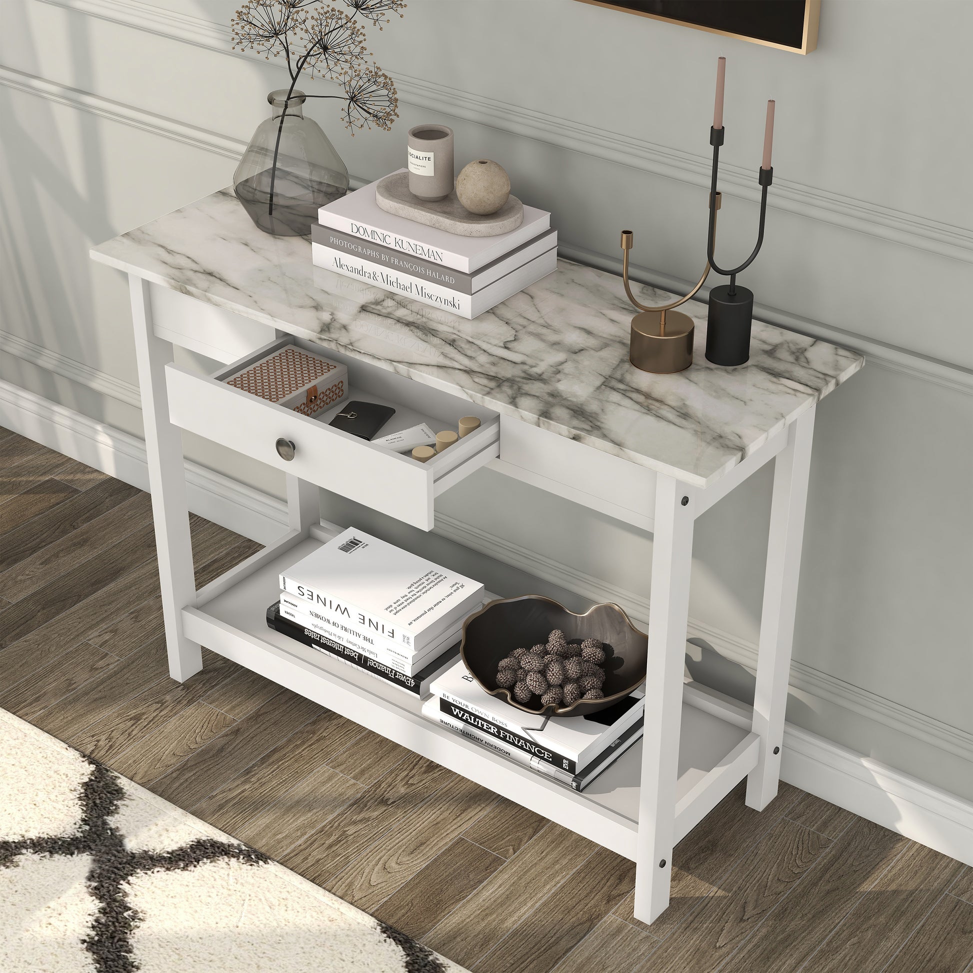 Left angled bird's eye view of a modern white and faux marble console table with a lower shelf and drawer open in a living area with accessories