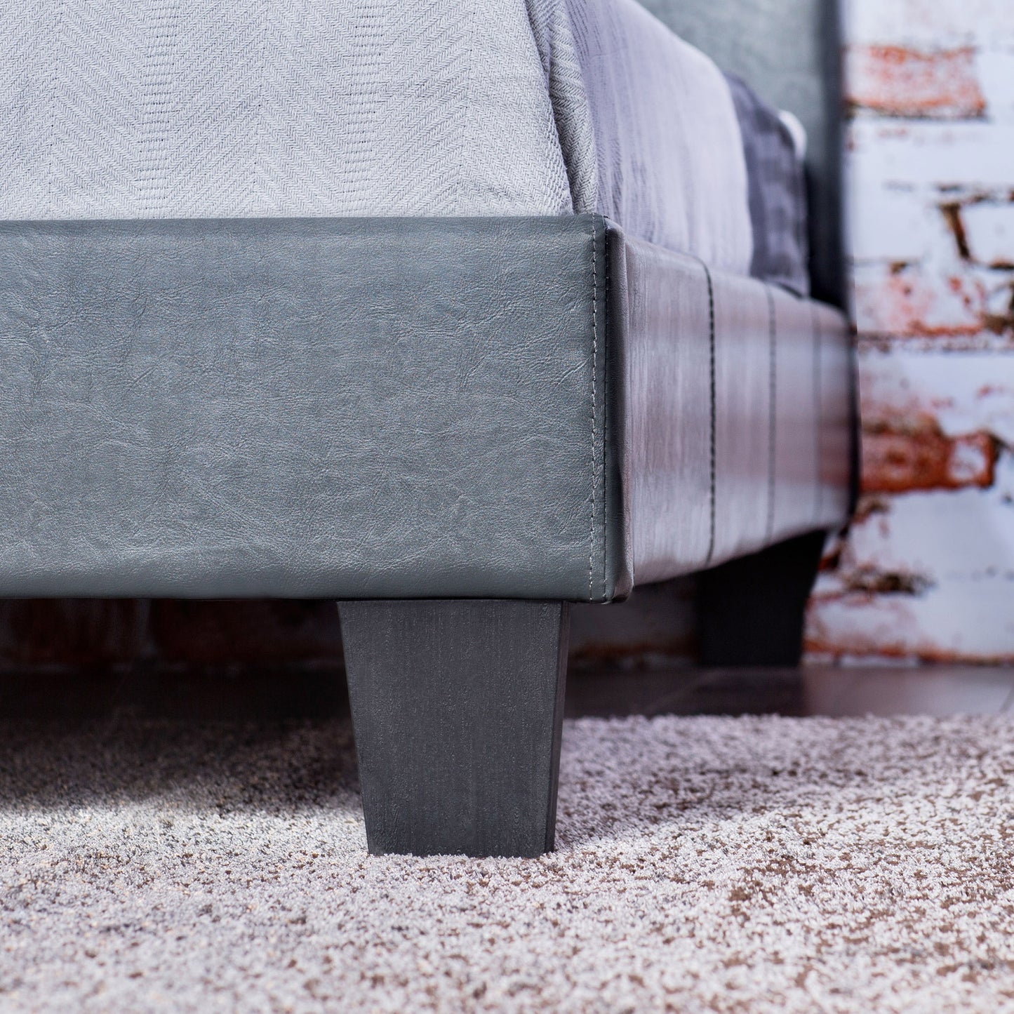 Left angled footboard/leg detail view of a contemporary gray faux leather full platform bed in a bedroom with accessories