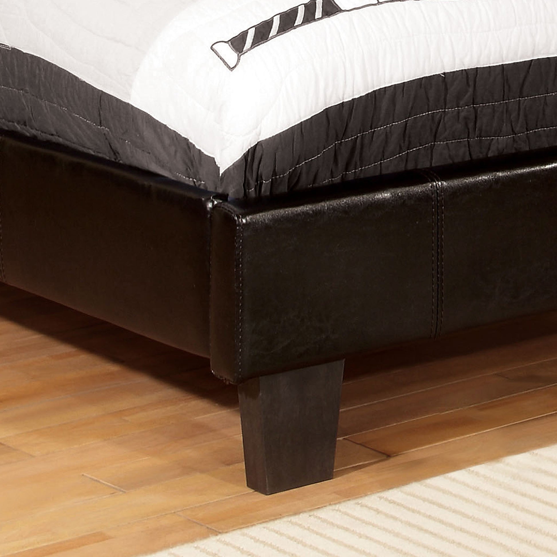 Right angled footboard/leg detail view of a contemporary espresso faux leather twin platform bed in a bedroom with accessories