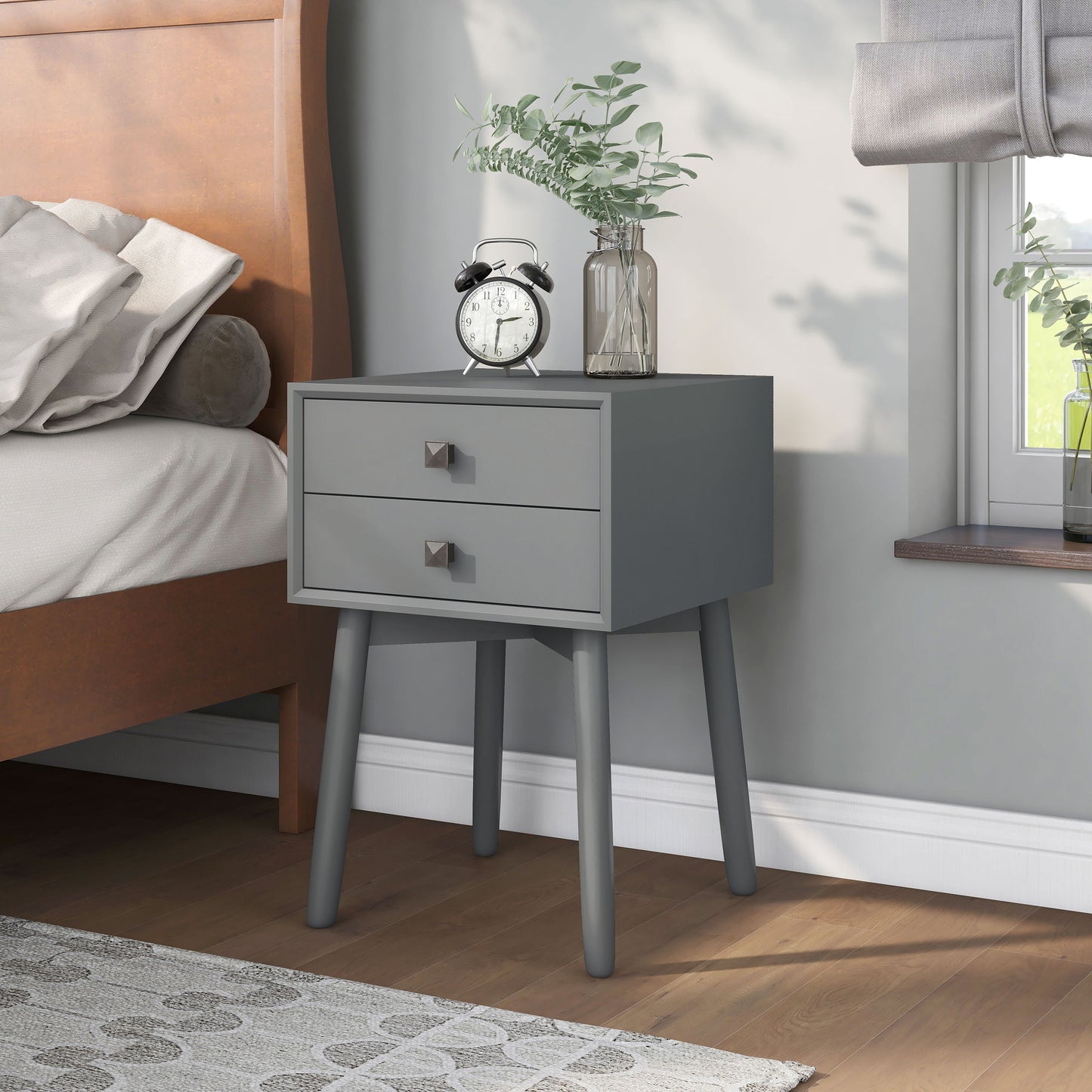 Left angled modern gray two-drawer compact nightstand with splayed legs in a bedroom with accessories