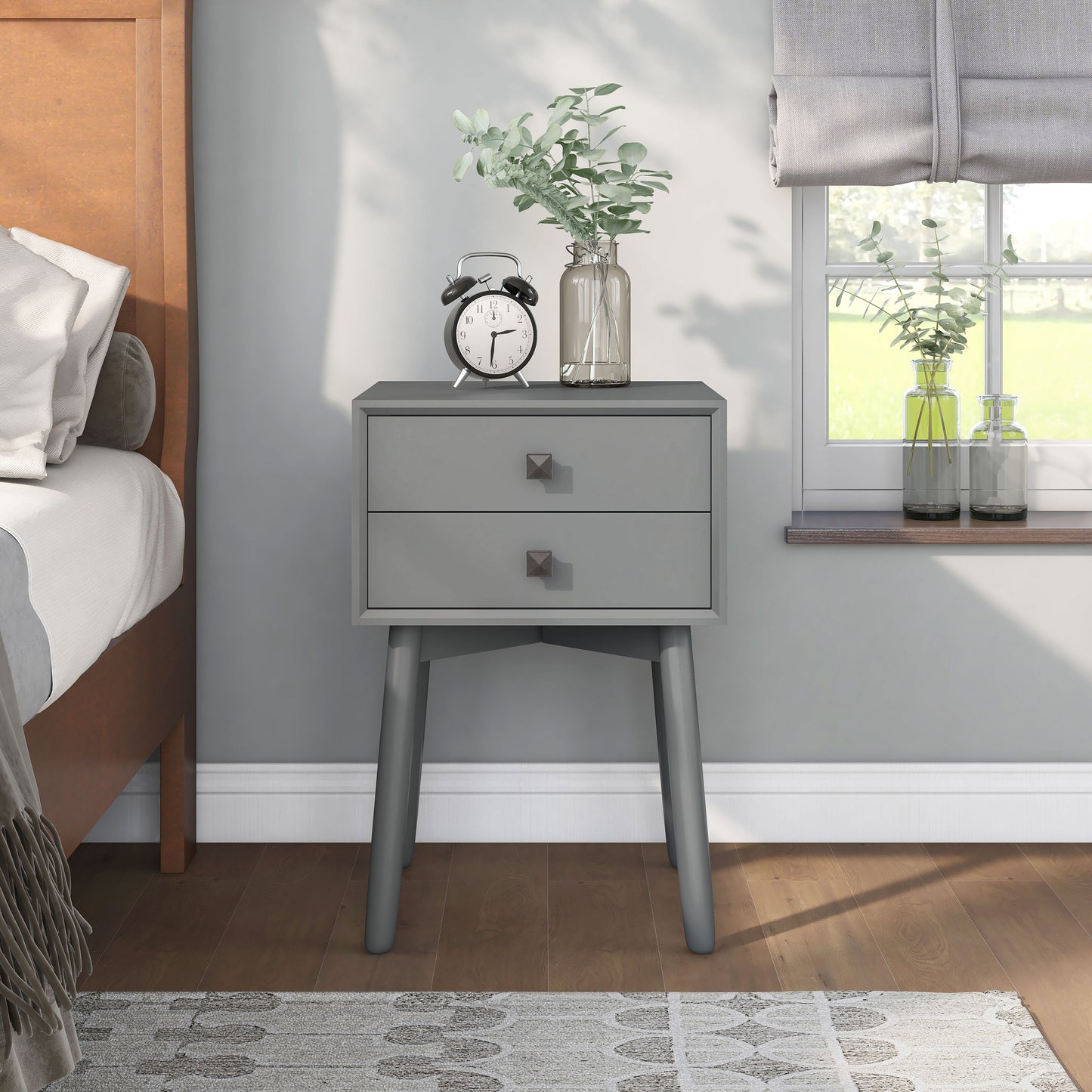 Front-facing modern gray two-drawer compact nightstand with splayed legs in a bedroom with accessories
