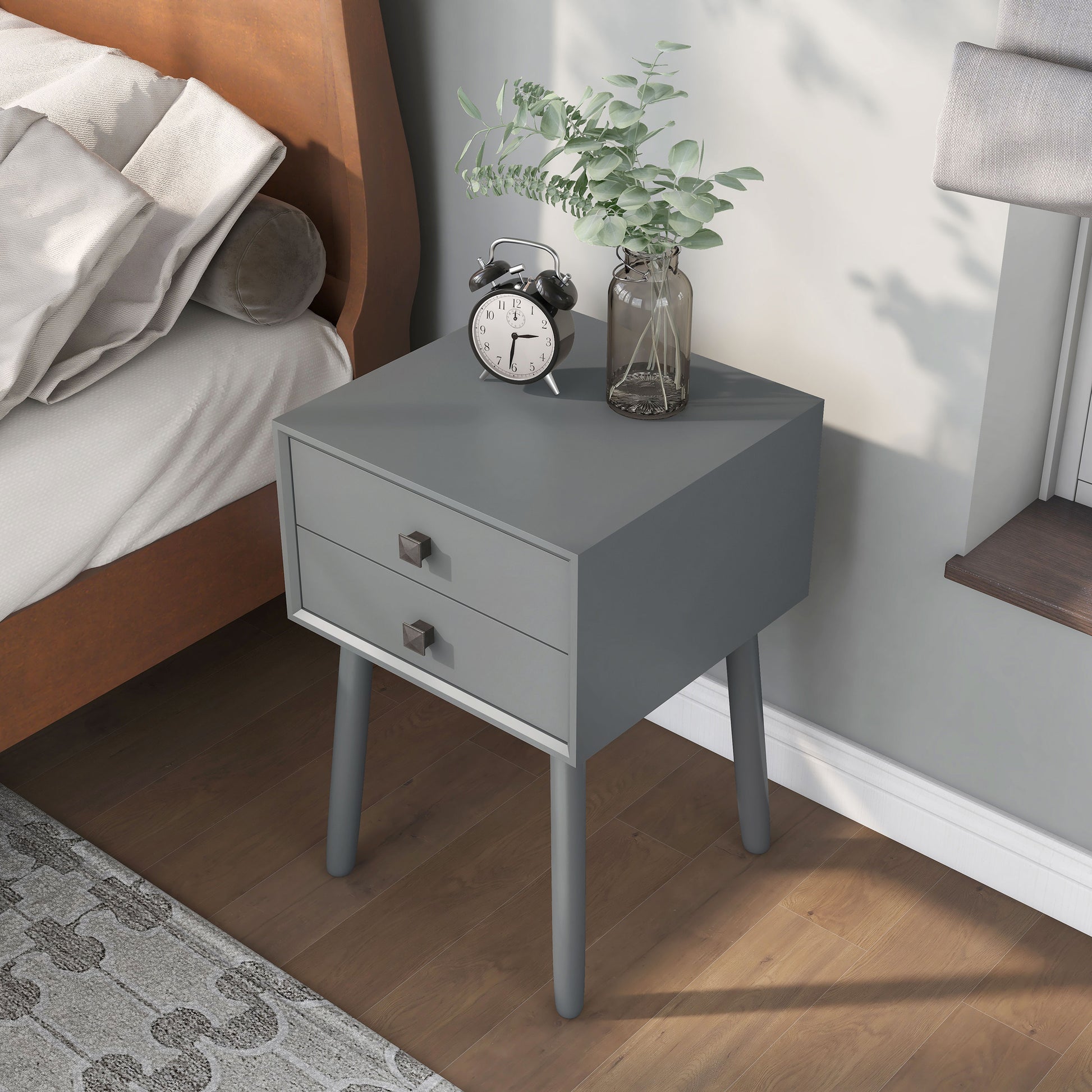 Left angled bird's eye view of a modern gray two-drawer compact nightstand with splayed legs in a bedroom with accessories