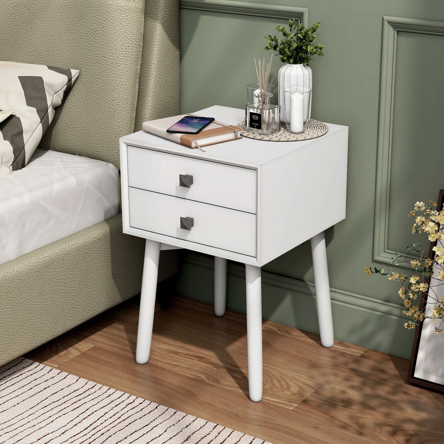 Left angled modern white two-drawer compact nightstand with splayed legs in a bedroom with accessories