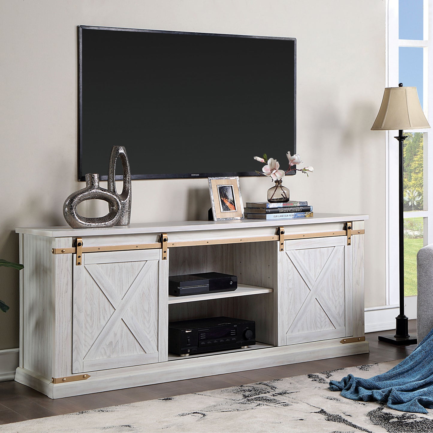 Left angled farmhouse white and gold sliding door TV stand in a living room with accessories