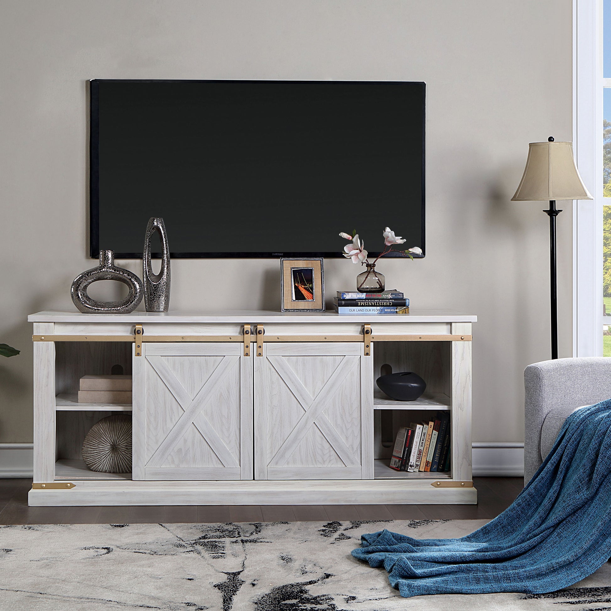 Front-facing farmhouse white and gold sliding door TV stand in a living room with accessories