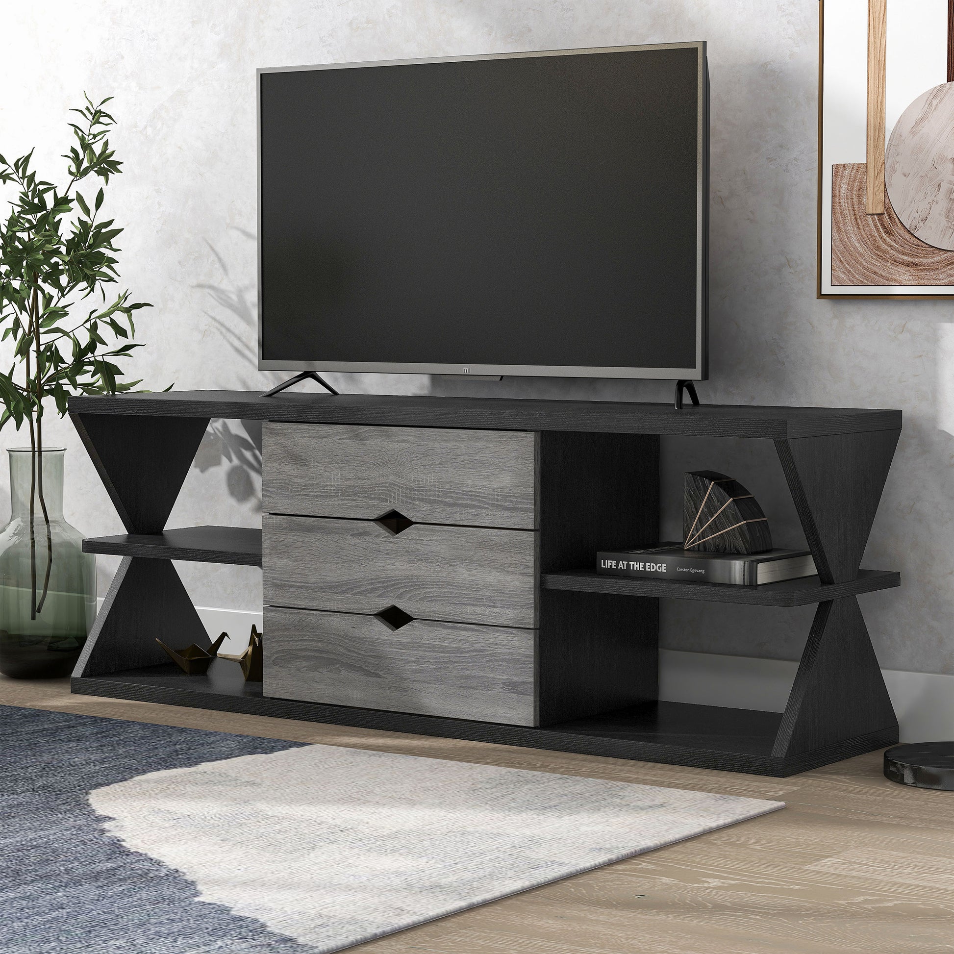 Left angled modern black and distressed gray three-drawer TV stand in a living area with accessories