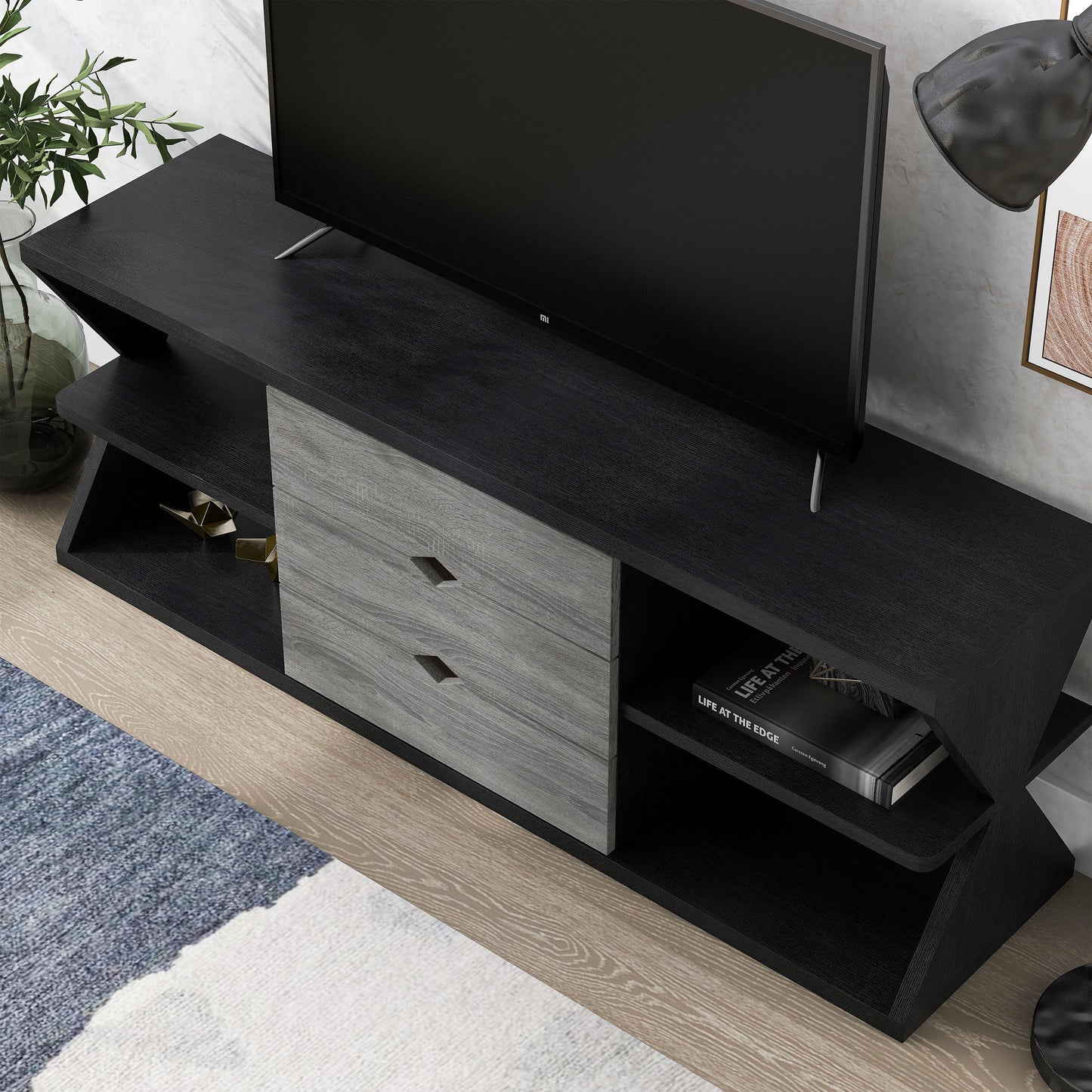 Left angled bird's eye view modern black and distressed gray three-drawer TV stand in a living area with accessories