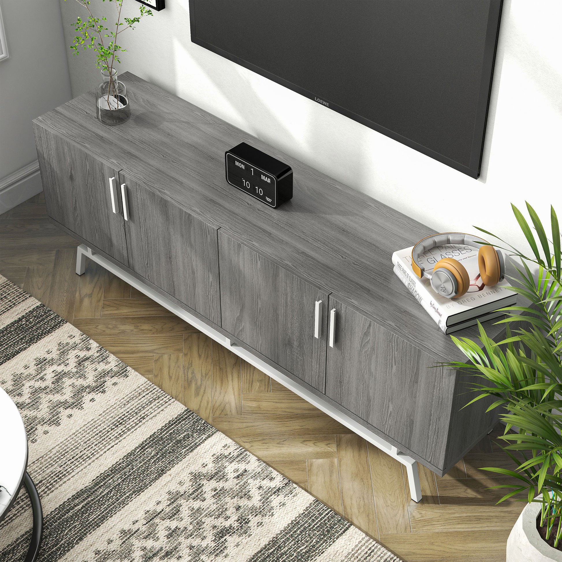 Left angled bird's eye view of a modern distressed gray and silver four-door TV stand in a living room with accessories