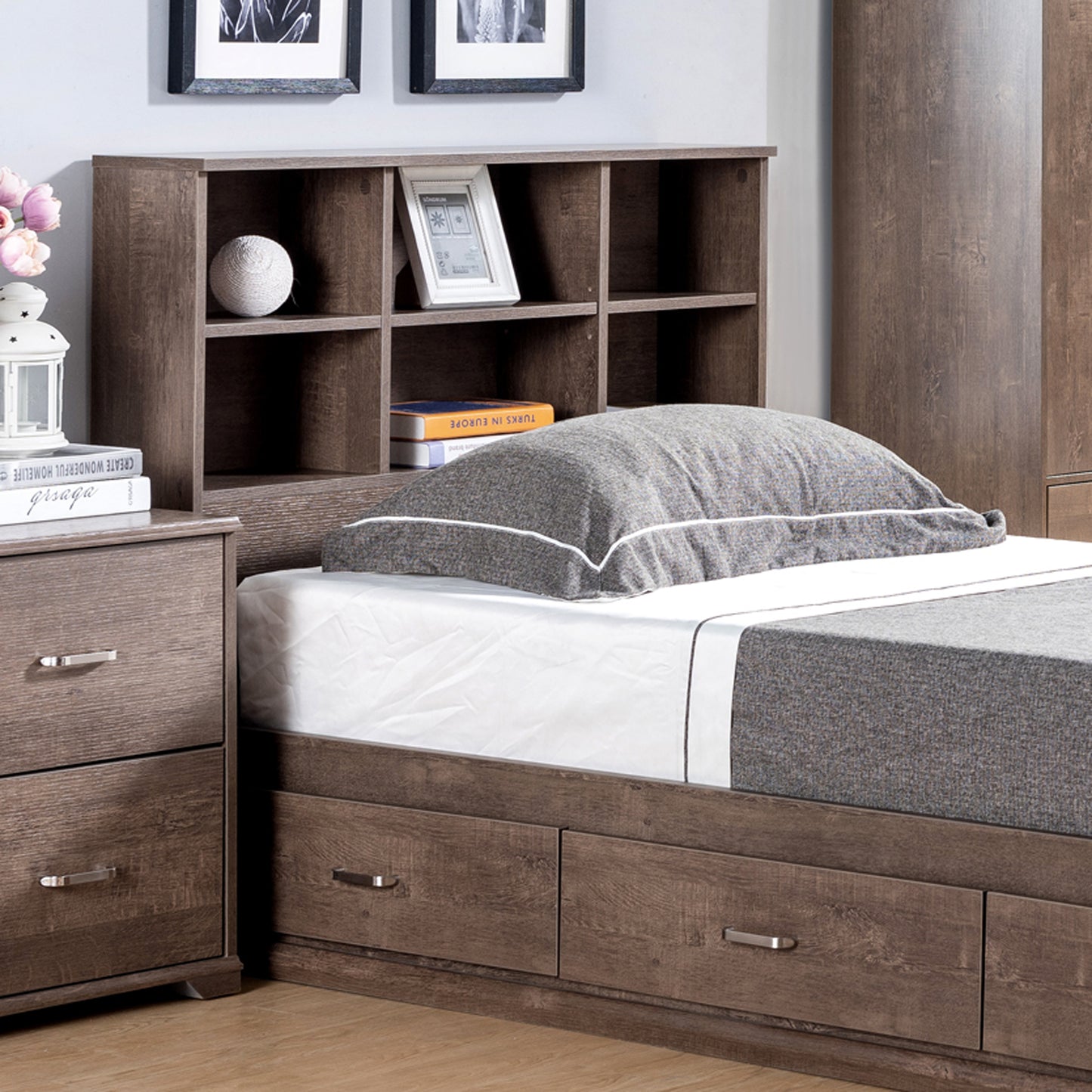 Right angled close-up of a contemporary walnut three-drawer platform storage bed with a bookcase headboard in a bedroom with accessories
