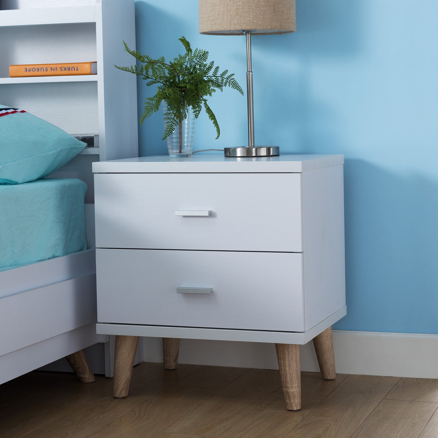 Left angled mid-century modern white two-drawer nightstand in a bedroom with accessories