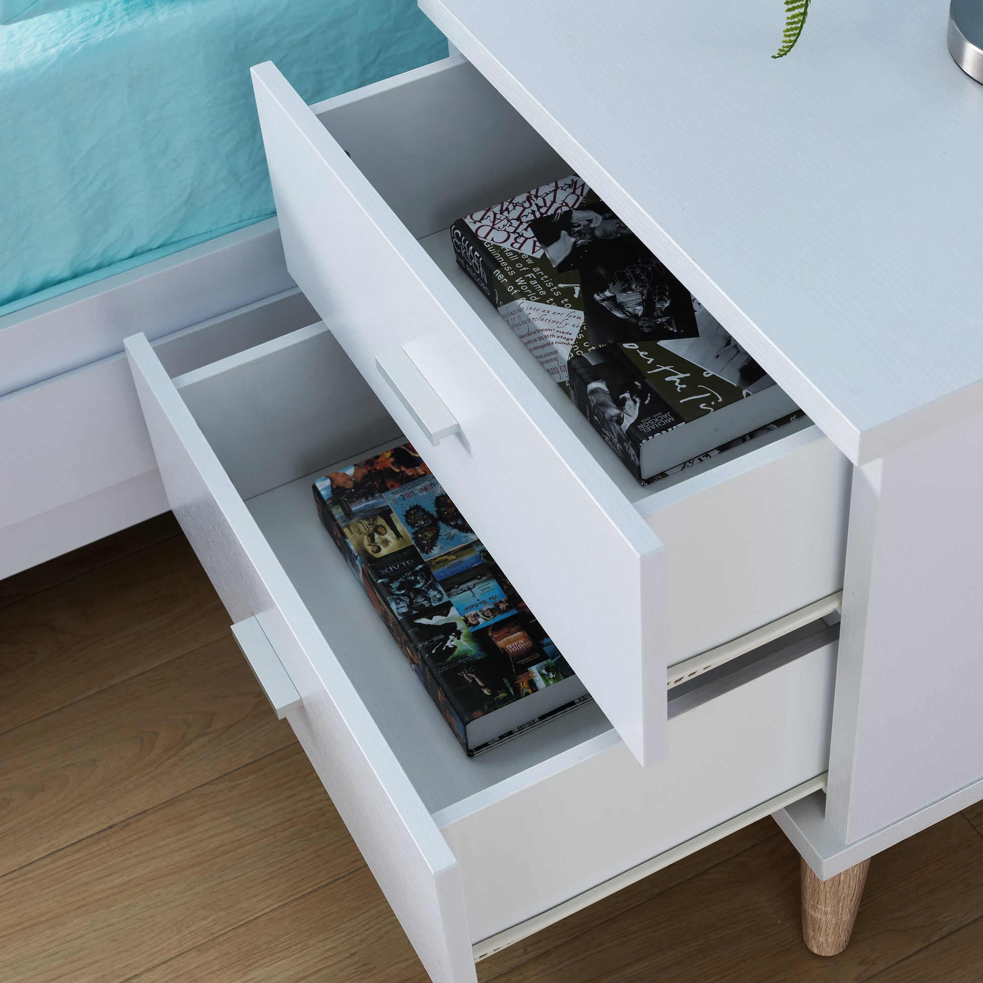 Left angled bird's eye view of a mid-century modern white two-drawer nightstand with drawers open in a bedroom with accessories