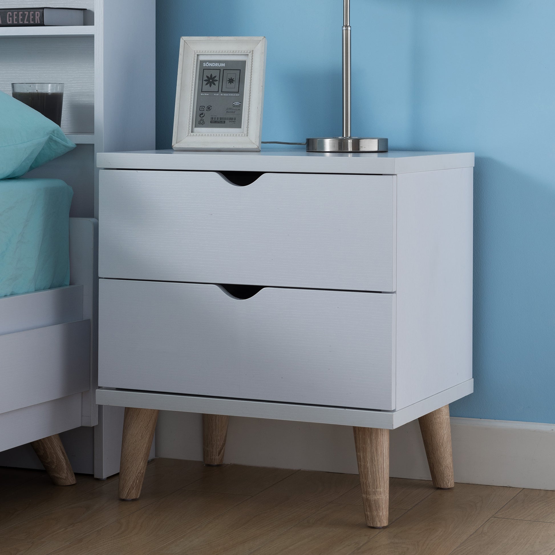 Left angled mid-century modern white two-drawer nightstand in a bedroom with accessories