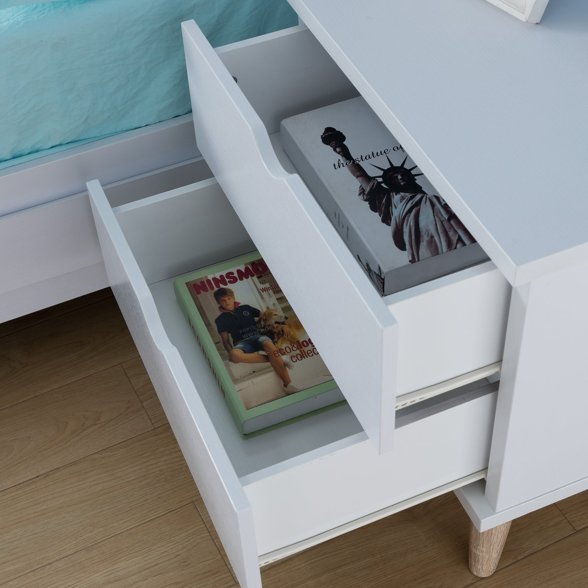 Left angled bird's eye view of a mid-century modern white two-drawer nightstand with drawers open in a bedroom with accessories