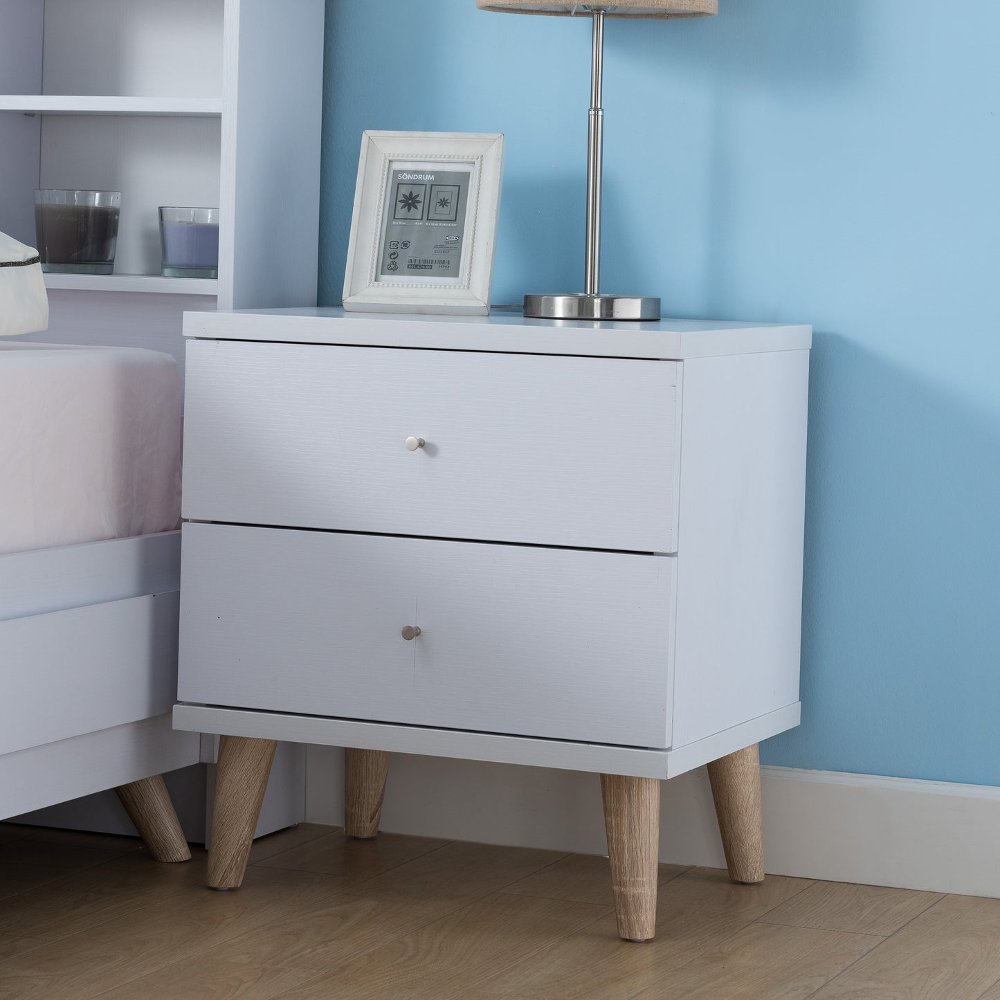 Left angled mid-century modern white two-drawer nightstand in a bedroom with accessories