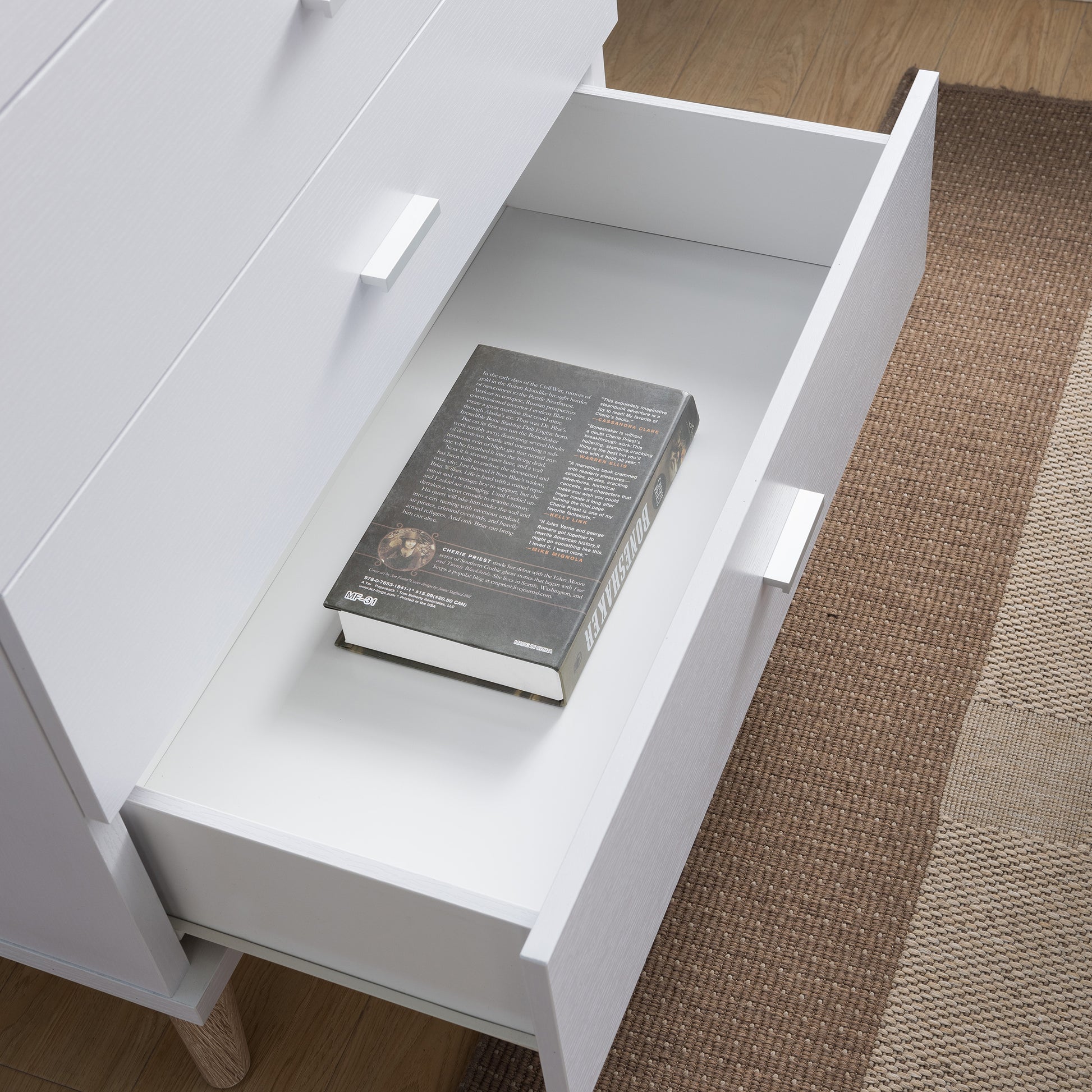 Right angled bird's eye close-up view of a mid-century modern white four-drawer chest dresser with the bottom drawer open in a bedroom with accessories