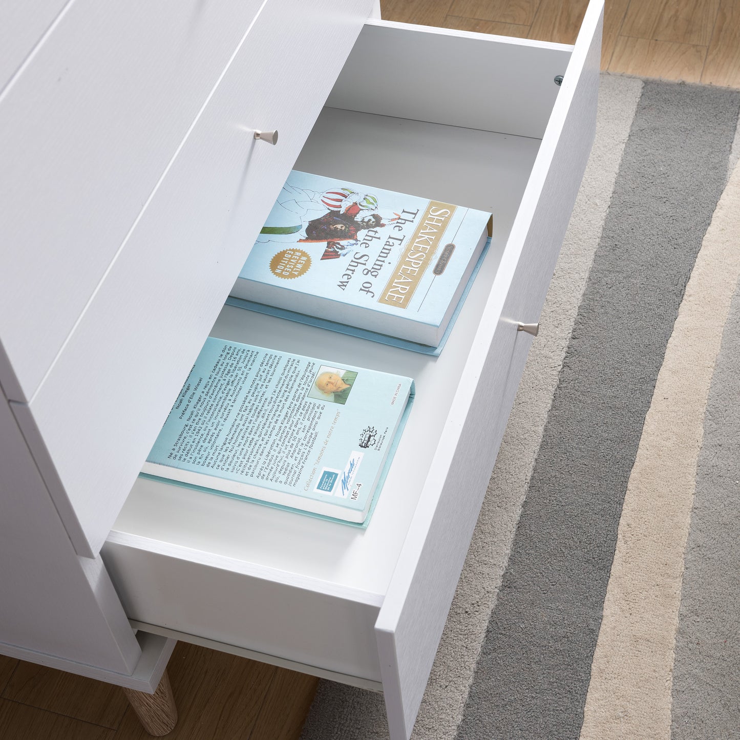 Right angled bird's eye close-up view of a mid-century modern white four-drawer chest dresser with the bottom drawer open in a bedroom with accessories