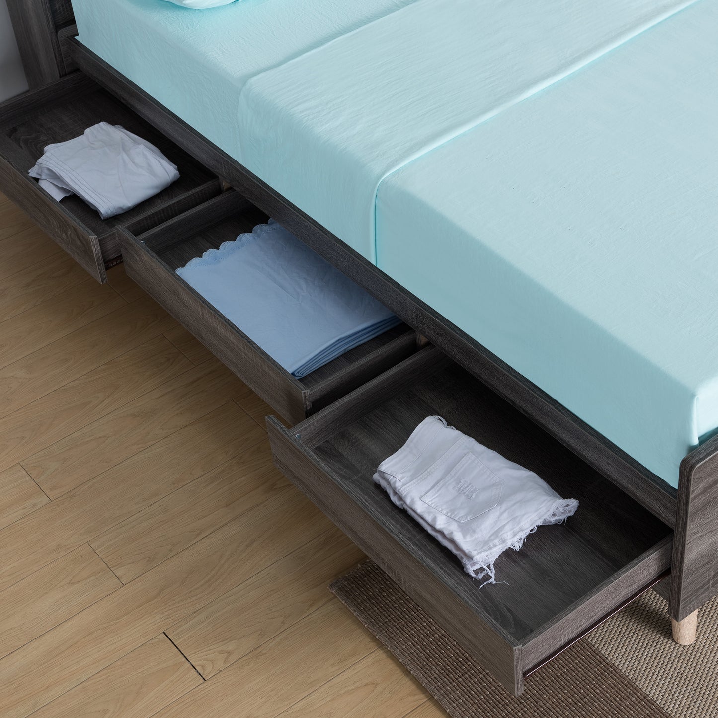 Right angled bird's eye close-up view of a mid-century modern distressed gray platform storage bed with three drawers open in a bedroom with accessories