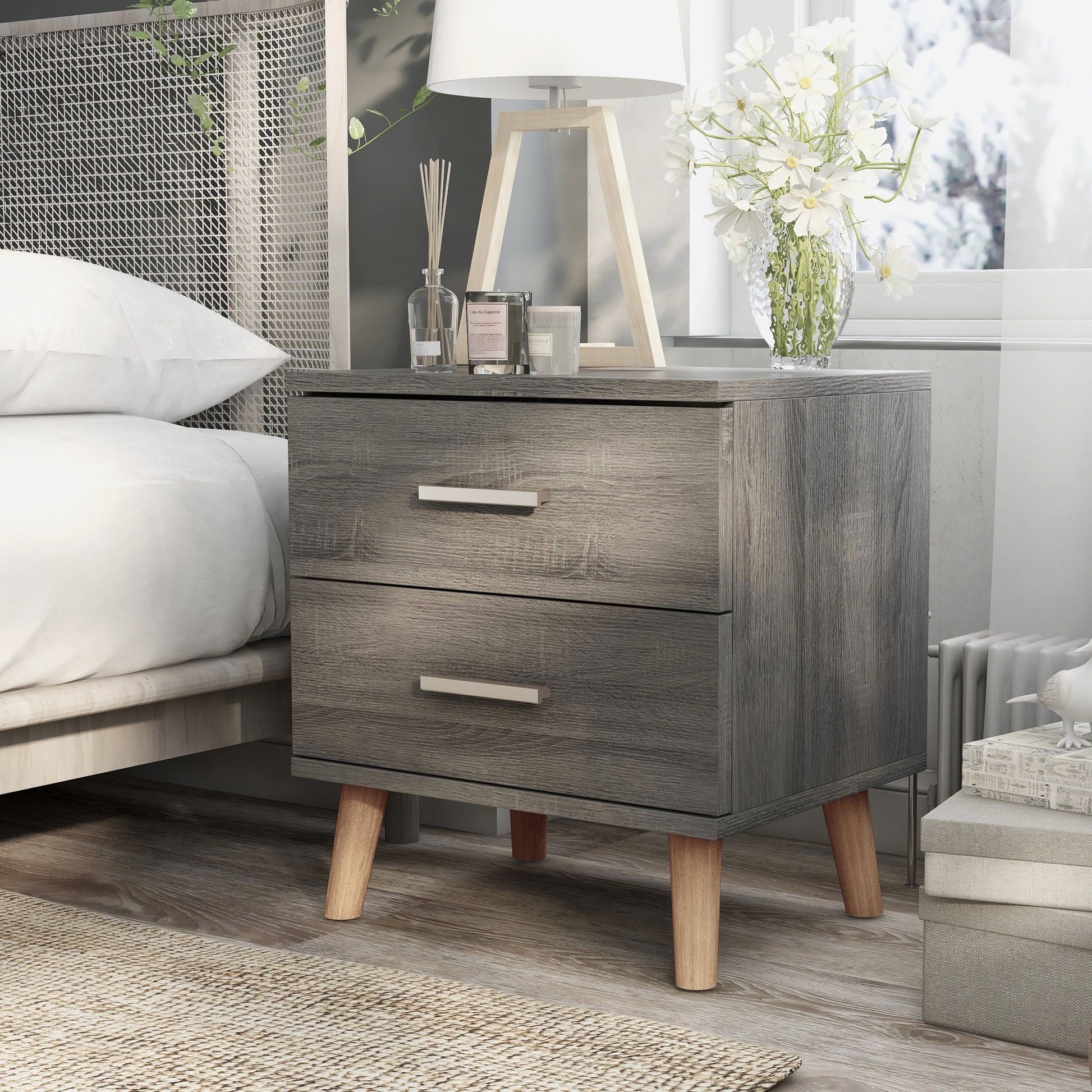 Left angled mid-century modern distressed gray two-drawer nightstand in a bedroom with accessories