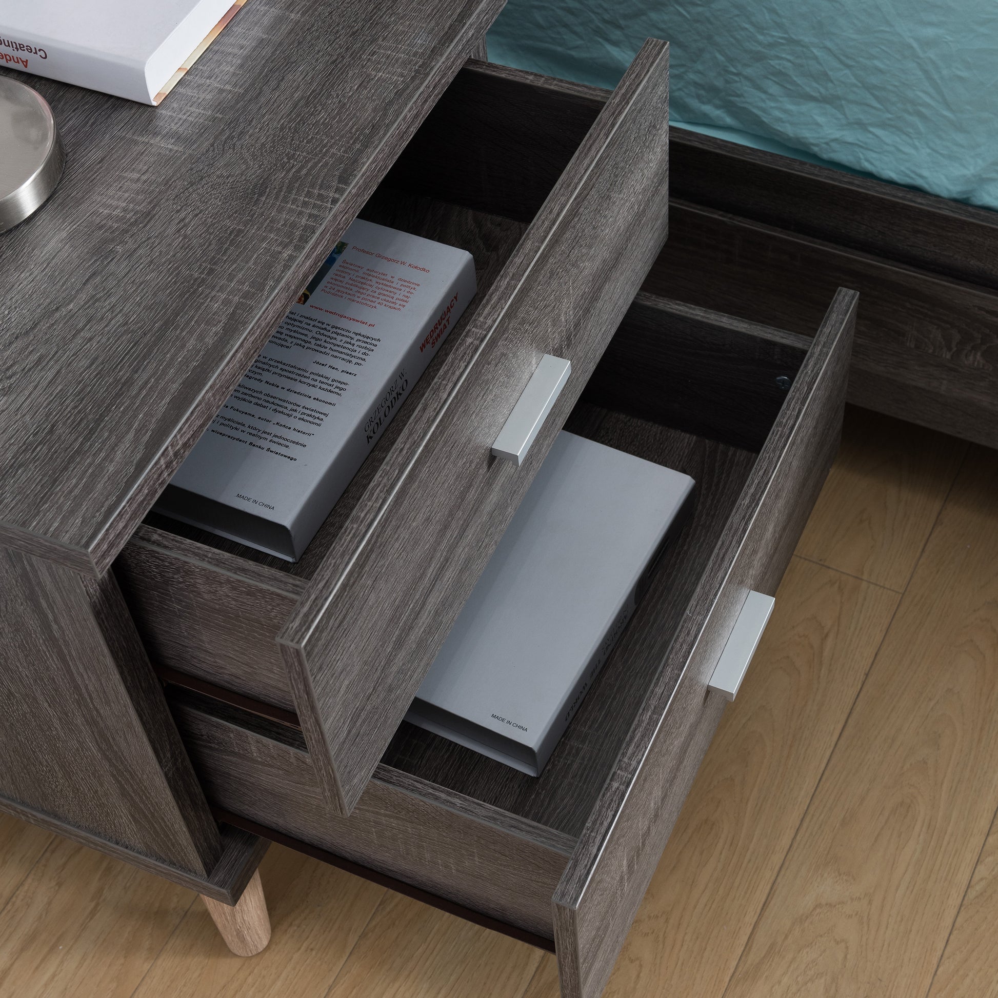 Right angled bird's eye view of a mid-century modern distressed gray two-drawer nightstand with drawers open in a bedroom with accessories