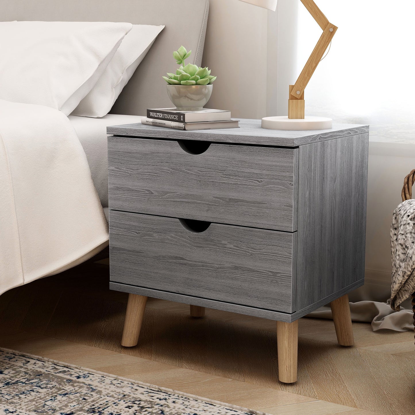 Left angled mid-century modern distressed gray two-drawer nightstand in a bedroom with accessories