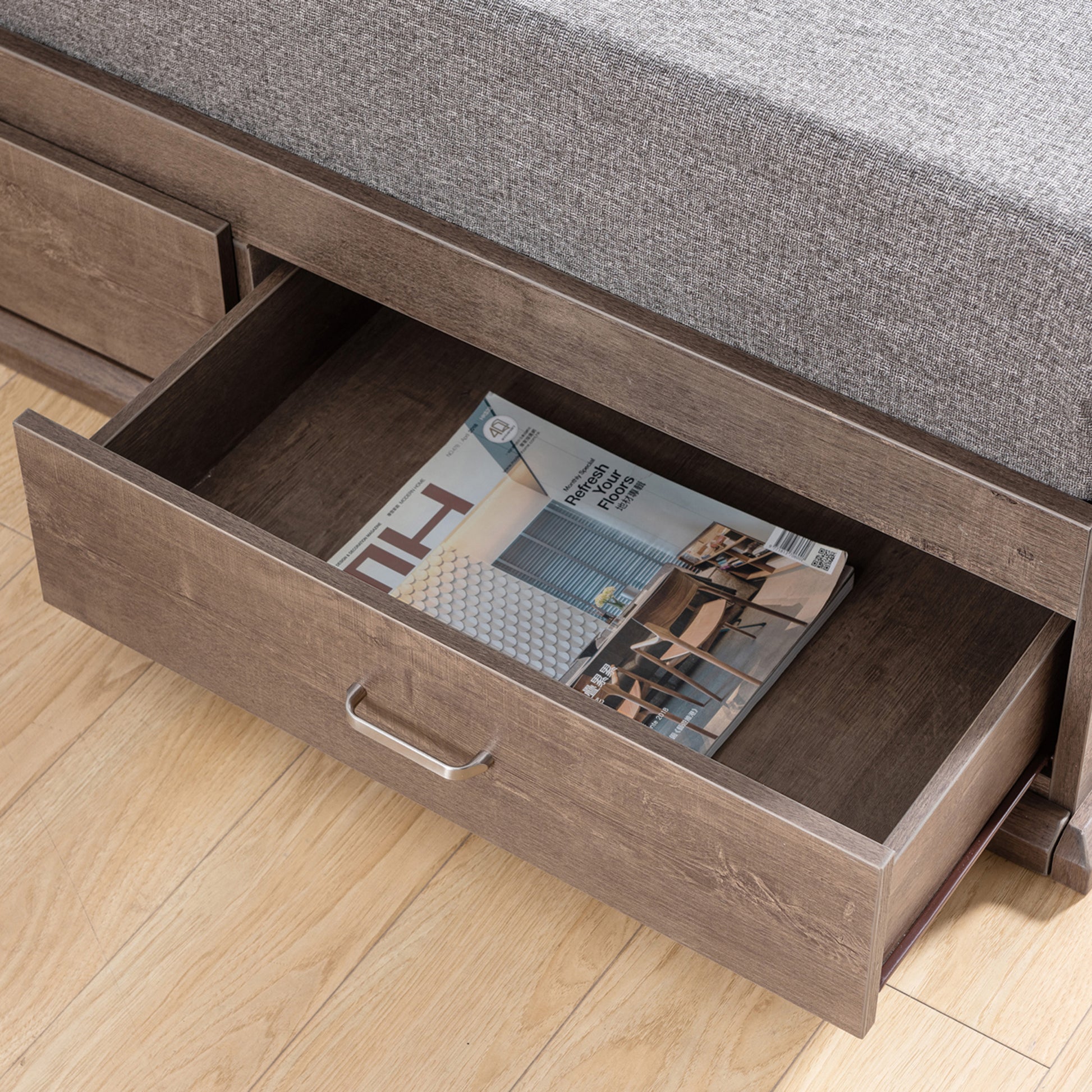 Right angled bird's eye close-up view of a contemporary walnut three-drawer platform storage bed with a drawer open in a bedroom with accessories