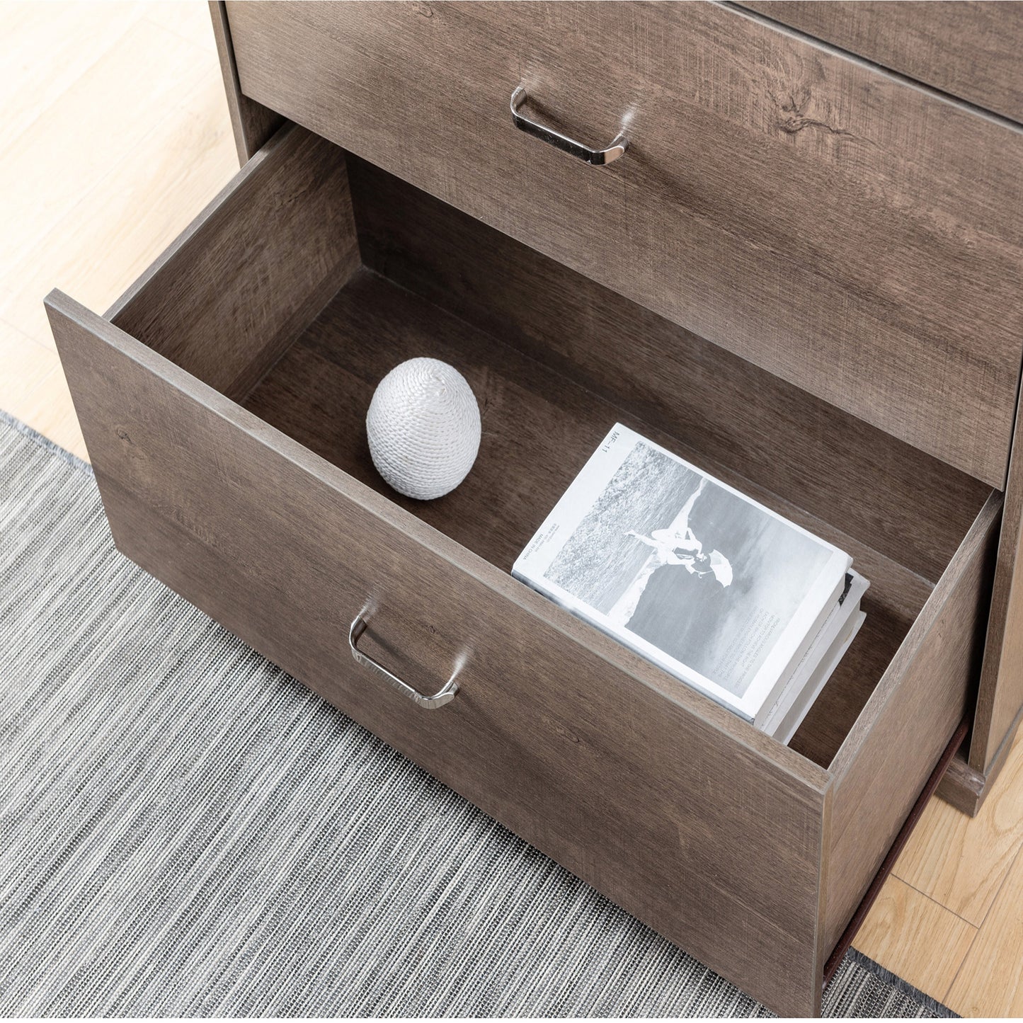Left angled bird's eye view of a contemporary walnut four-drawer chest dresser with bottom drawer open in a bedroom with accessories