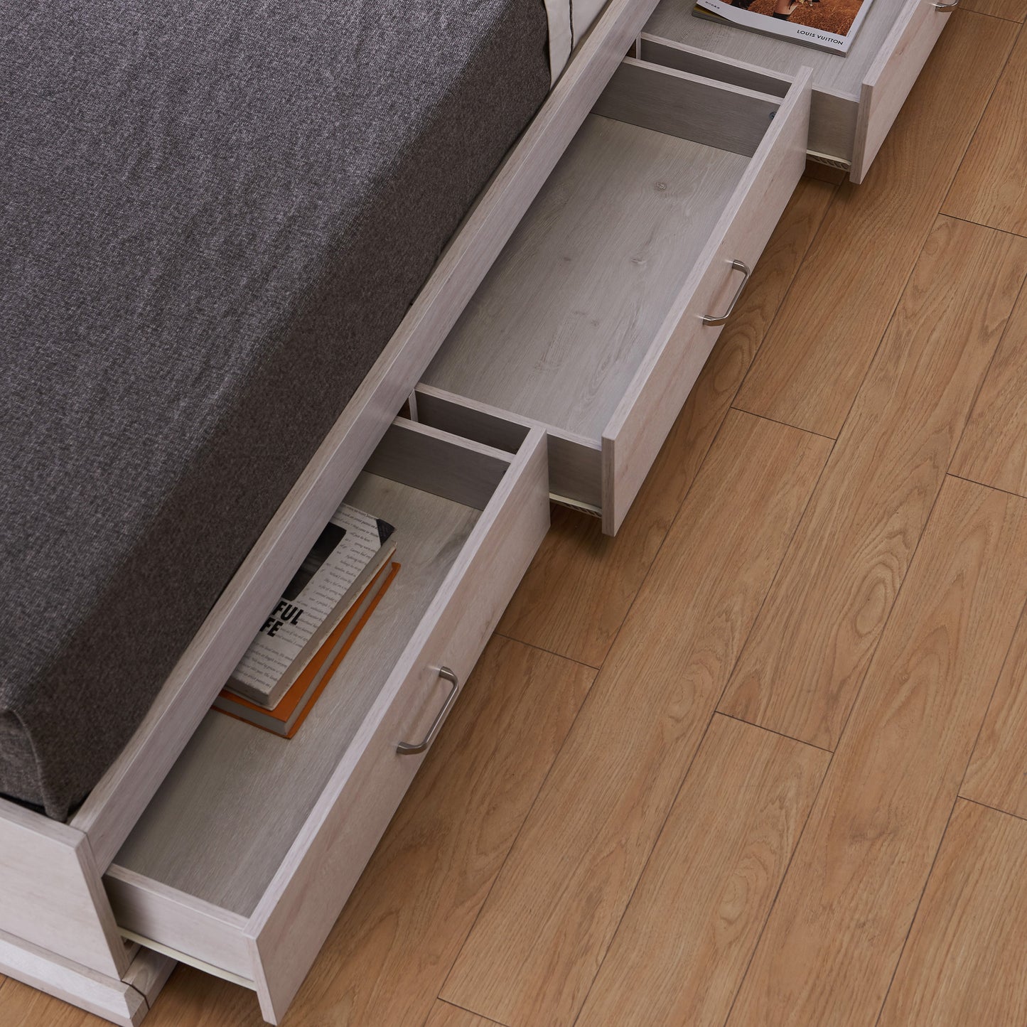 Left angled bird's eye close-up view of a contemporary white oak three-drawer platform storage bed with drawers open in a bedroom with accessories
