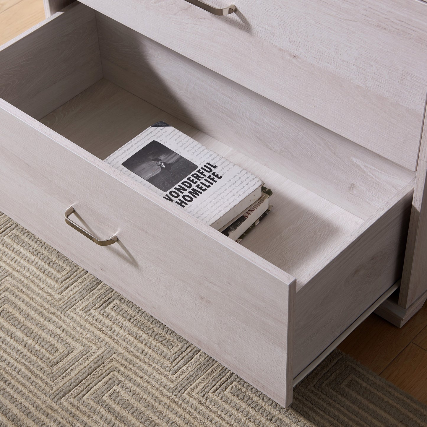 Left angled close-up view of a contemporary white oak four-drawer chest dresser with bottom drawer open with a rug and accessories
