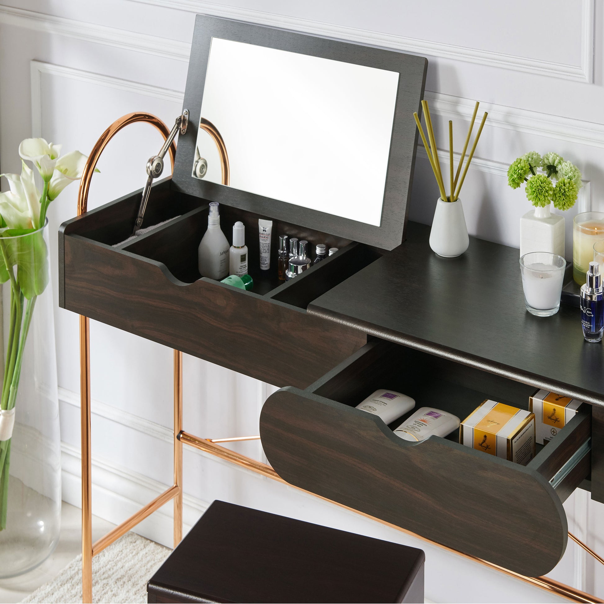 Left angled close-up of a modern glam walnut and gold lift-top vanity table with top lifted to show mirror and drawer open in a living area with accessories