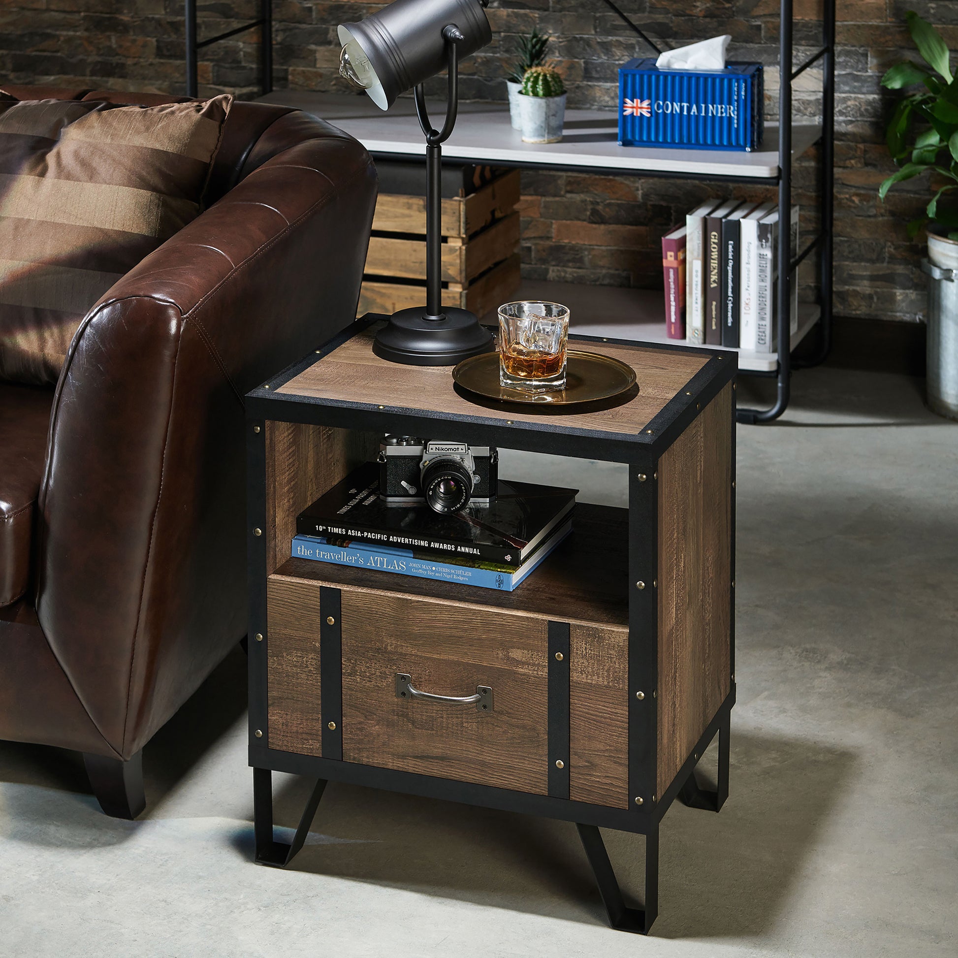 Left angled industrial reclaimed oak and black one shelf one drawer end table in a living room with accessories