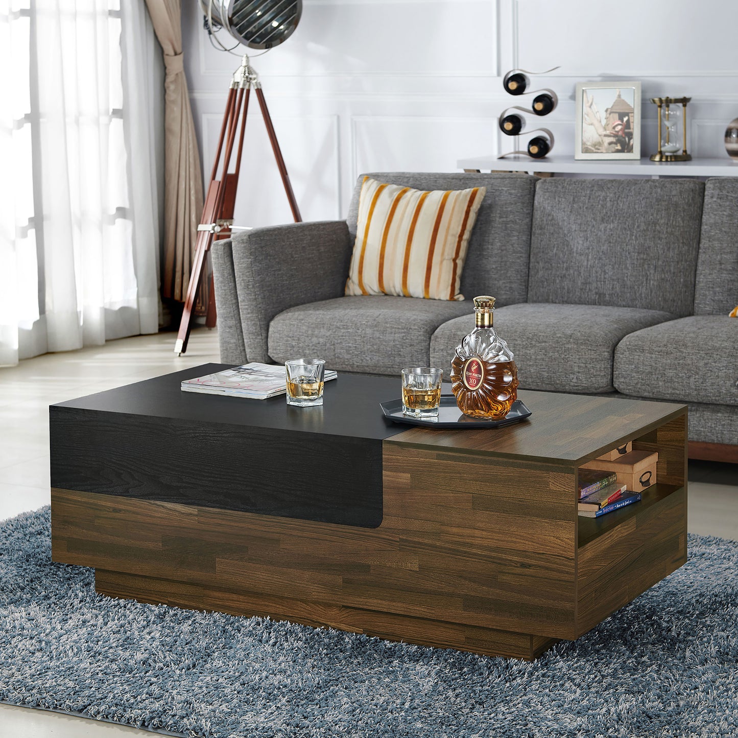 Left angled contemporary light hickory and black sliding top one-drawer coffee table in a living room with accessories