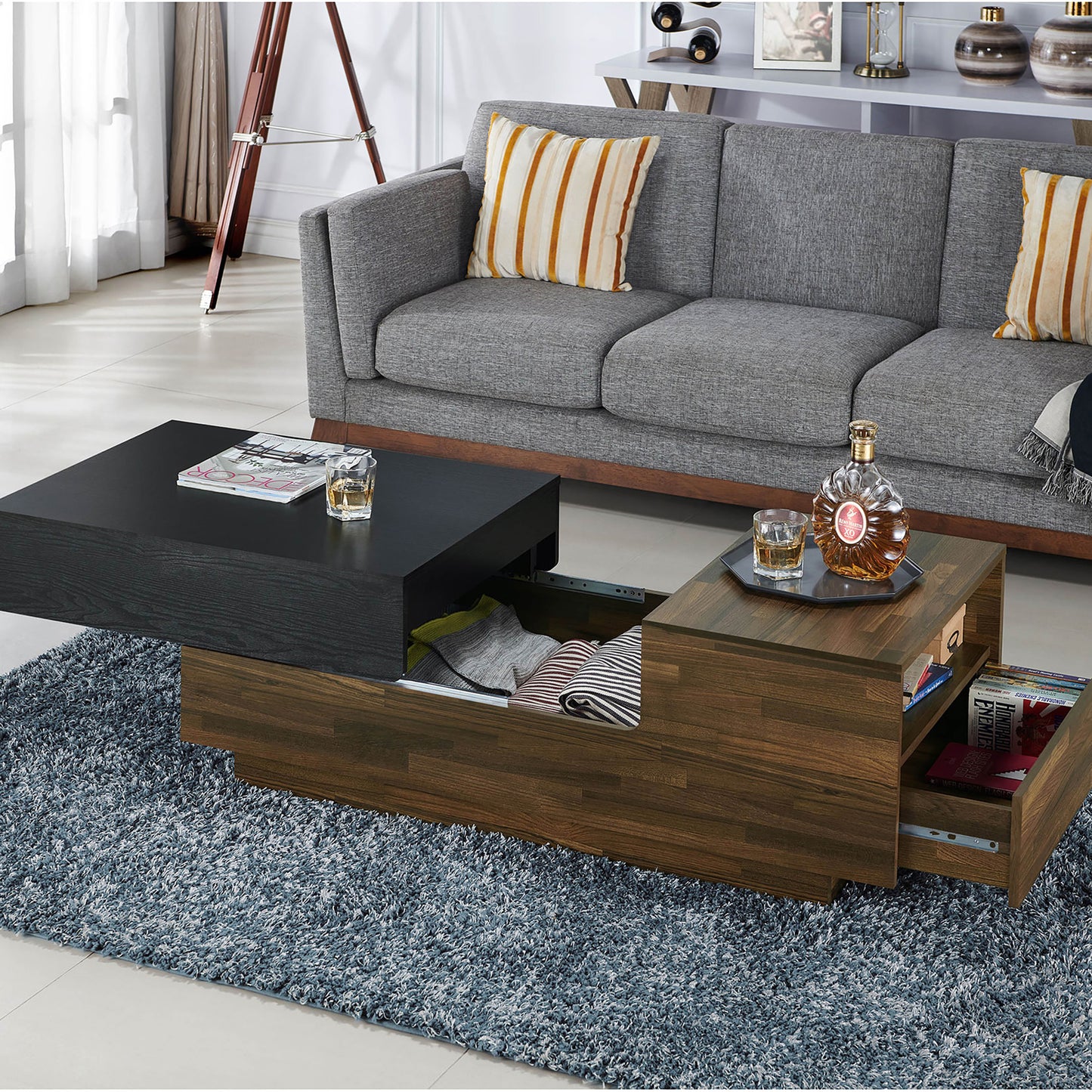 Left angled contemporary light hickory and black sliding top one-drawer coffee table with top and drawer open in a living room with accessories