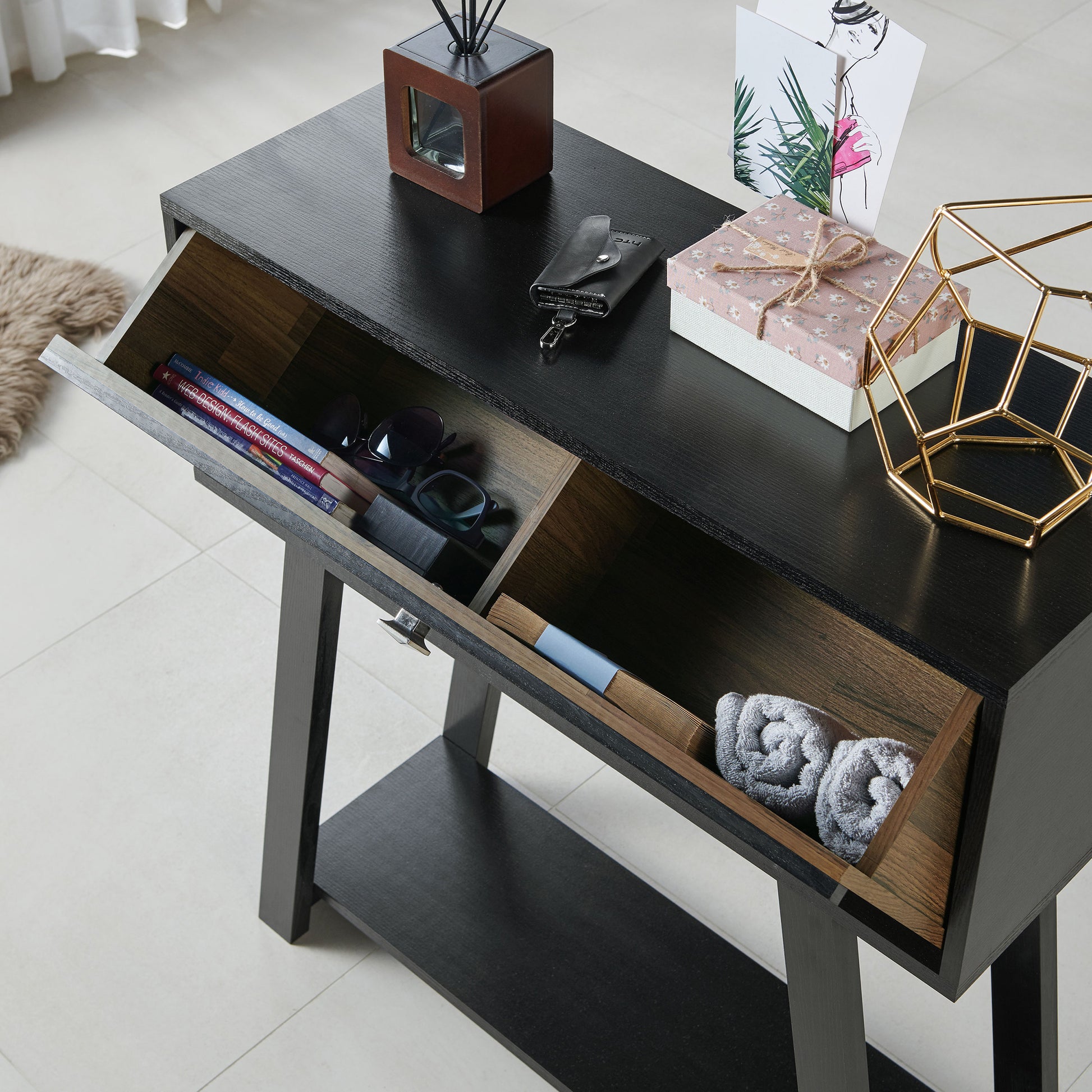 Left angled bird's eye view of a modern black and wood one-drawer console table with a shelf with drawer open in a living room with accessories