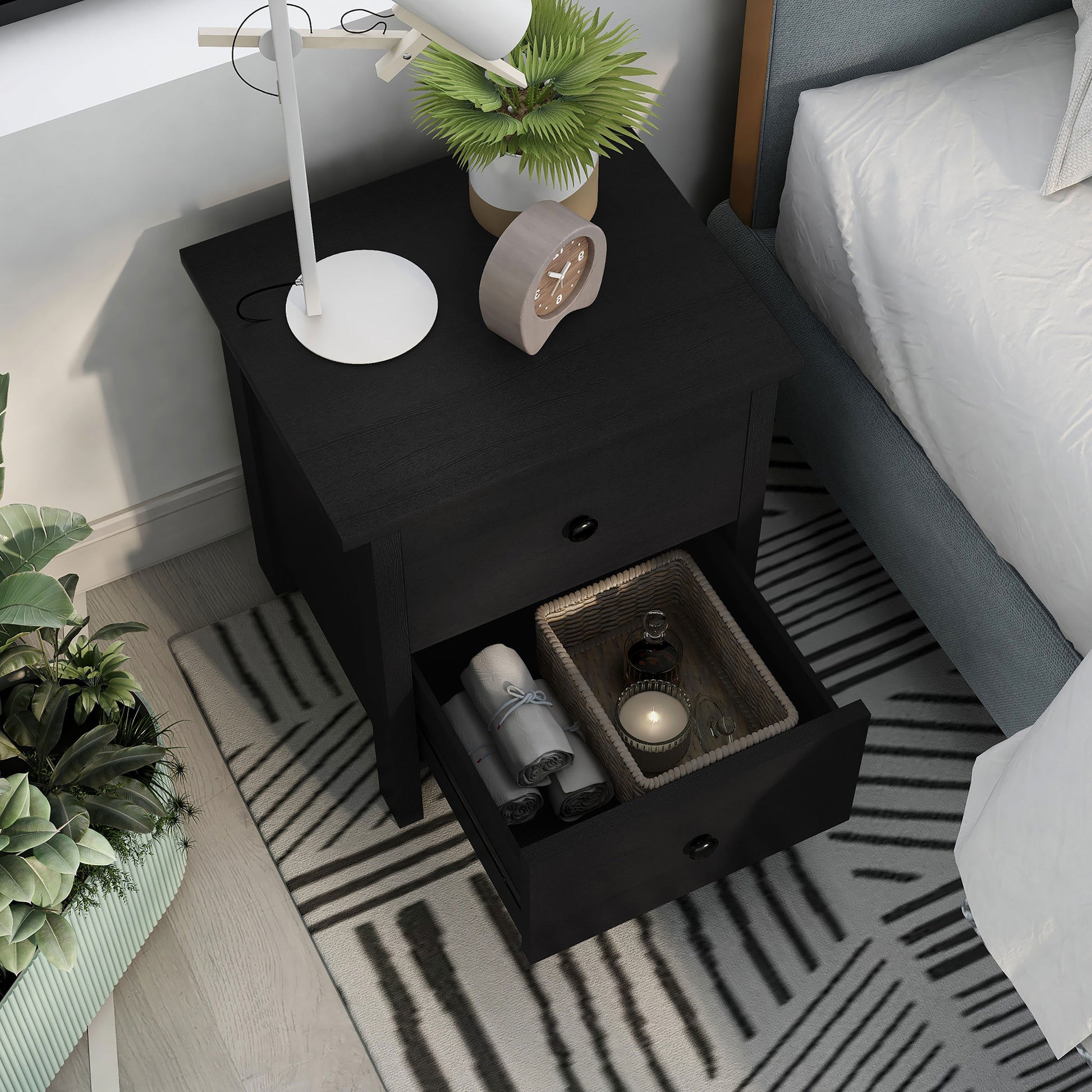 Right angled bird's eye view of a transitional black two-drawer nightstand with bottom drawer open in a bedroom with accessories