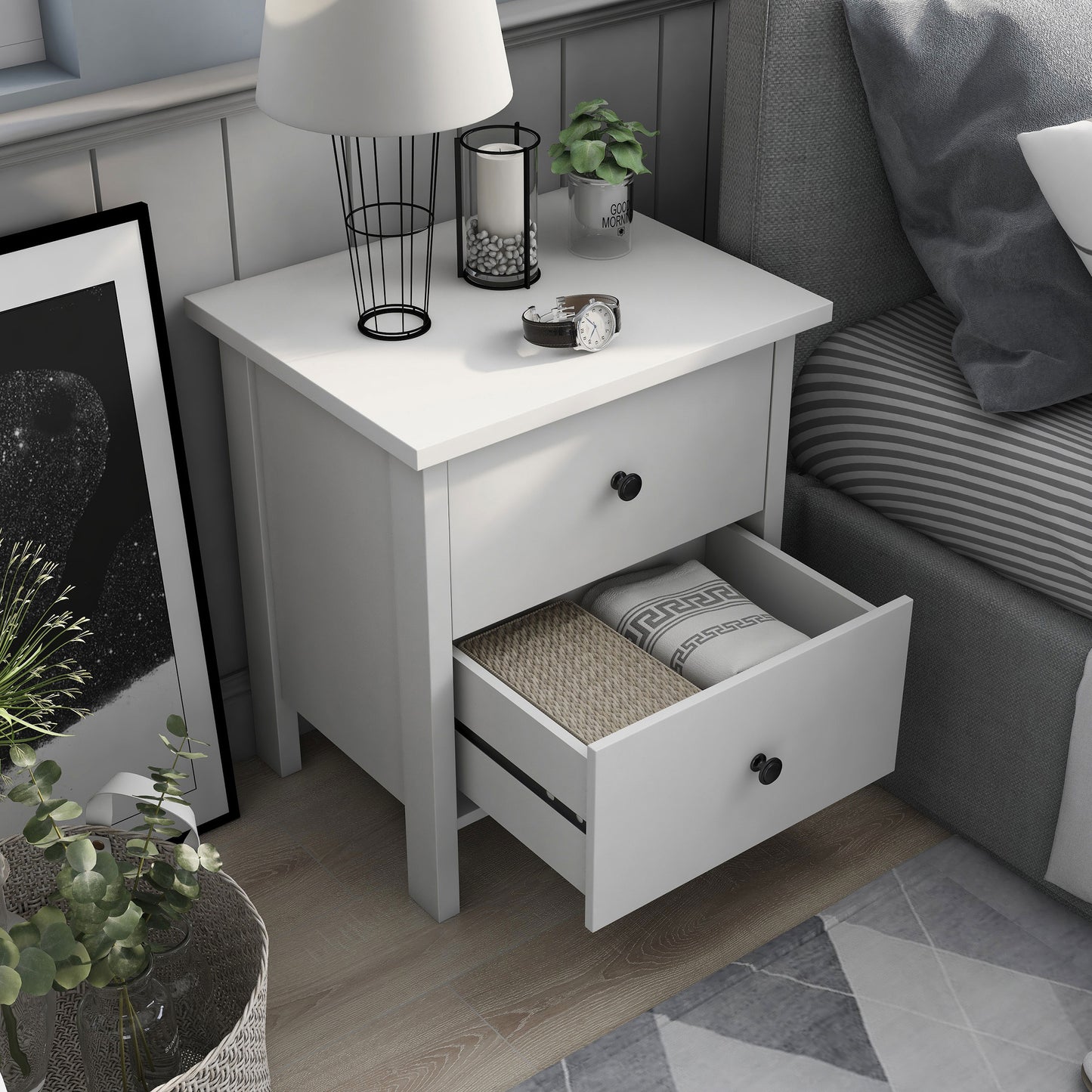 Right angled bird's eye view of a transitional white two-drawer nightstand with bottom drawer open in a bedroom with accessories