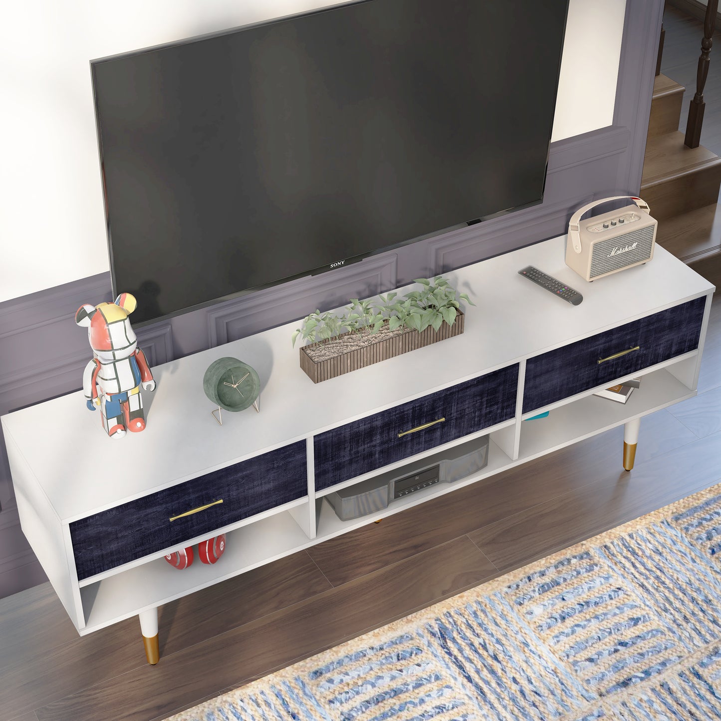 Right angled bird's eye view of a mid-century modern rustic navy blue and white three-shelf three-drawer TV stand in a living area with accessories